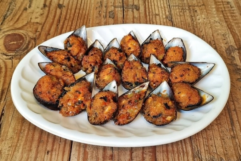 Mejillones rellenos crujientes y dorados sobre una bandeja