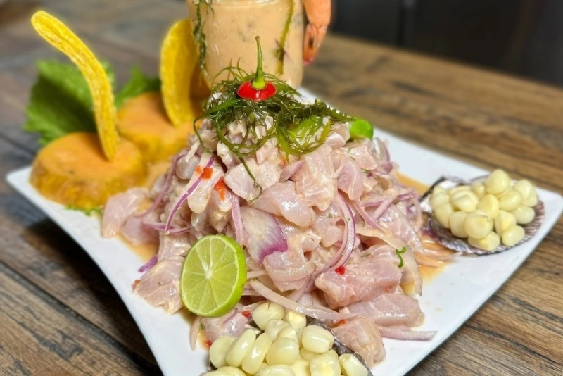 Plato de ceviche de bonito con cebolla roja, ají limo, camote y choclo sobre fondo neutro.