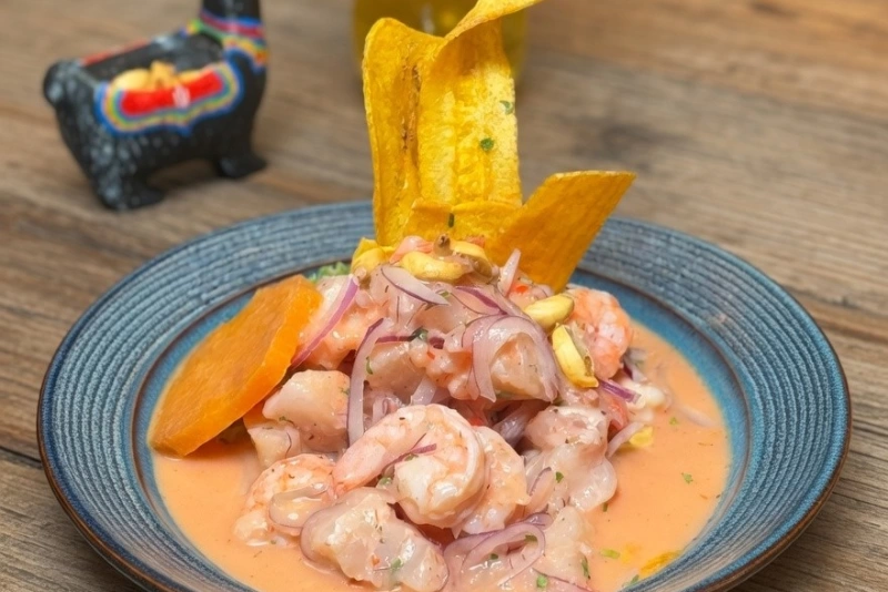 Ceviche de camarones frescos con cebolla roja, ají limo, cilantro y camote en un plato azul.