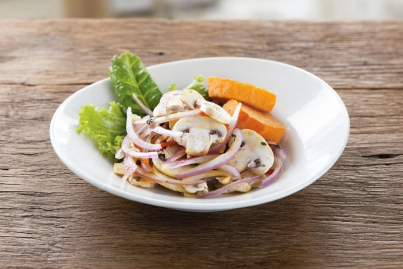 Ceviche de champiñones frescos marinado con limón, cebolla roja y ají en un bol de cerámica.
