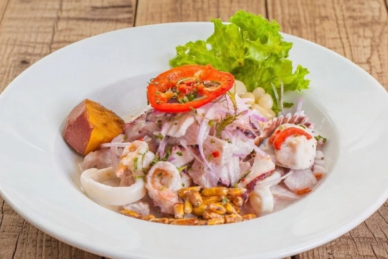 Ceviche mixto fresco con pescado, pulpo, langostinos, cebolla roja, camote y choclo en un plato.
