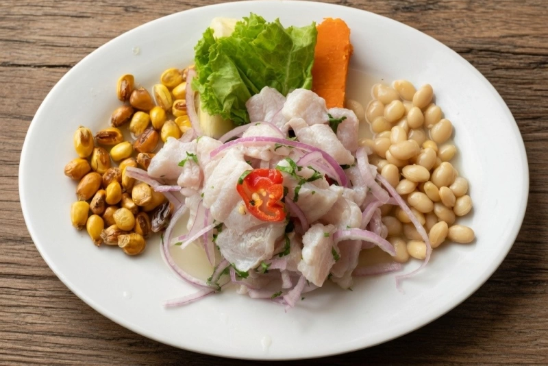 Plato de ceviche piurano con trozos de pescado fresco, zarandaja, chifles y ají limo rojo.