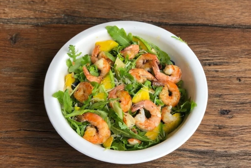 Ensalada de camarones frescos con aguacate, tomate y lechuga en un bol de madera rústico.