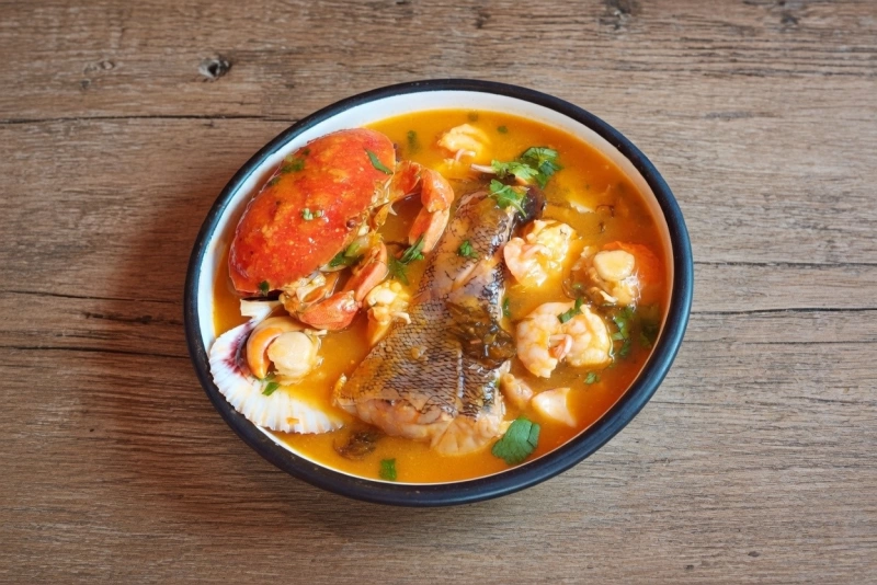 Gran plato de parihuela de pescado y mariscos con langostinos, choros y cangrejo en caldo rojo.