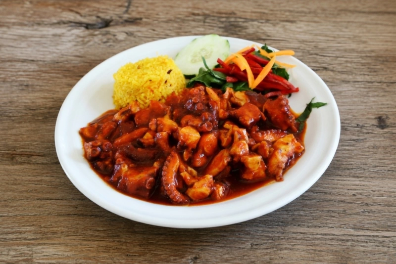 Plato de pulpo a la diabla en salsa roja espesa con rodajas de aguacate y arroz blanco al lado.