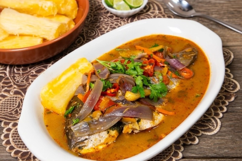 Sudado de pescado jugoso con cebolla roja, tomate, ají amarillo y yucas en un plato hondo blanco.
