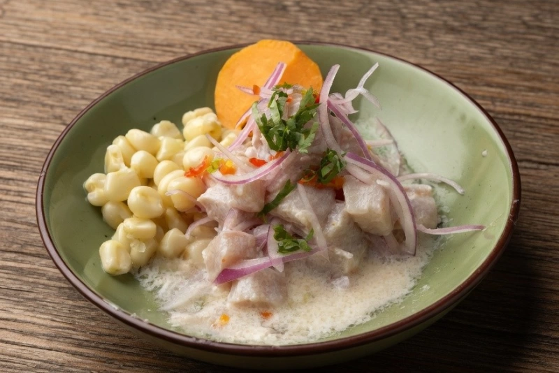 Delicioso Plato de ceviche de jurel fresco con cebolla morada, ají limo y camote en mesa rústica.